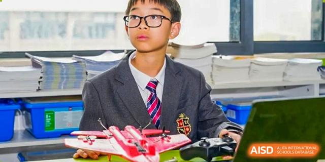 A student at HAILIANG FOREIGN LANGUAGE SCHOOL looks at the camera while holding a device for a robotics project.