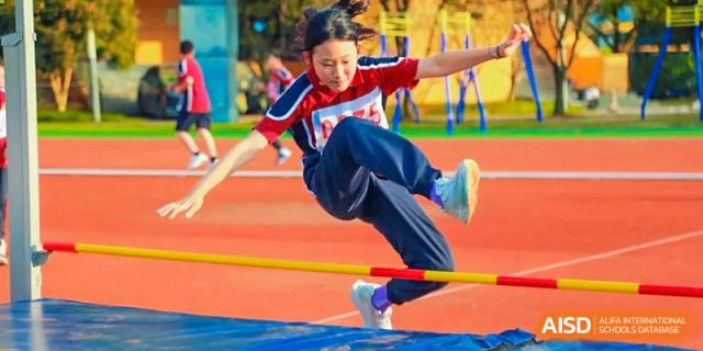 A female student at HAILIANG FOREIGN LANGUAGE SCHOOL jumps over a hurdle during a track and field event.