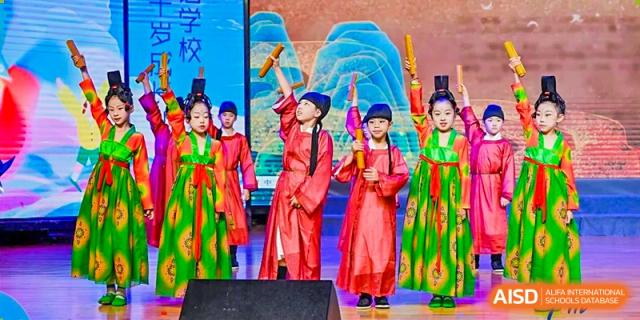 Students at HAILIANG FOREIGN LANGUAGE SCHOOL perform in traditional costumes on a stage with a scenic backdrop.