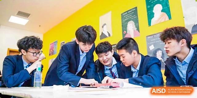 Four male students in school uniforms collaborating and looking at a notebook at HD Qingdao School.