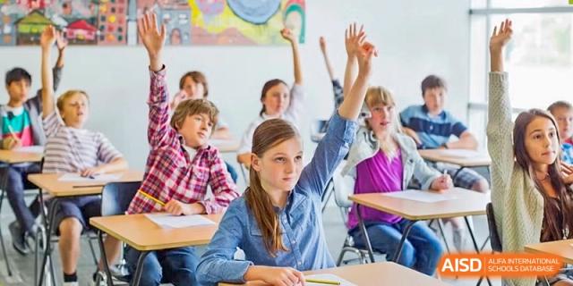 A classroom of students raising their hands to answer a question, with one girl in the foreground at HD Qingdao School.