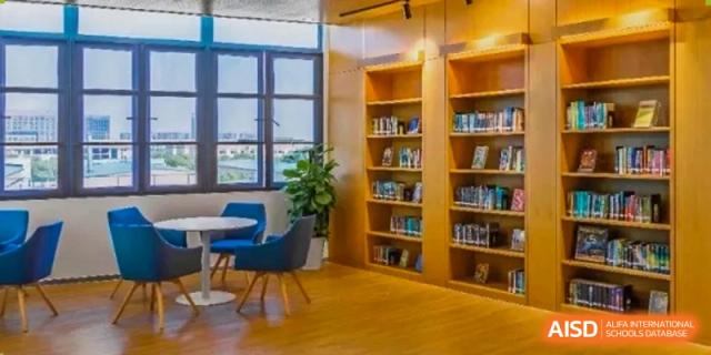 A cozy library with a tall bookshelf filled with books and a comfortable chair at HD Qingdao School.