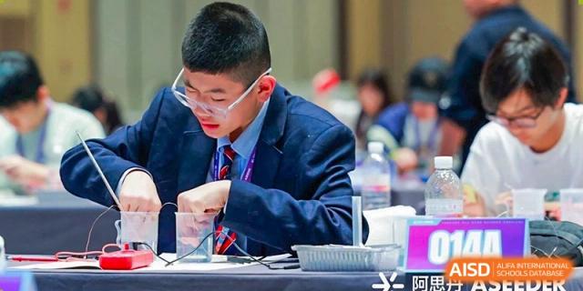 A male student in uniform writing or drawing intently at a desk at HD Qingdao School.