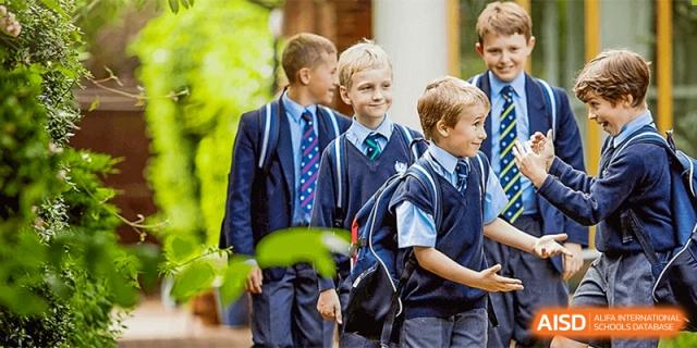 Three male students in uniform smiling while standing outdoors with their backpacks at HD Qingdao School.