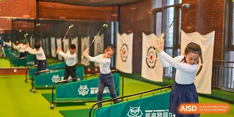 A male student in a white polo shirt swinging a golf club in an indoor practice range with a target and screen behind him HD Qingdao School.