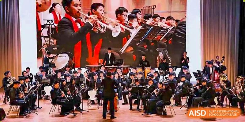A student orchestra with a mix of male and female students playing brass, woodwind, and string instruments HD Qingdao School.