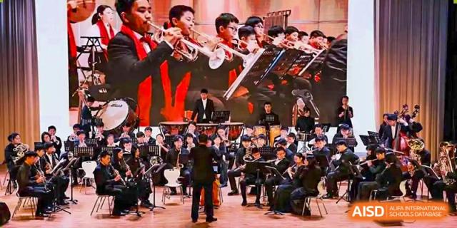 A student orchestra with a mix of male and female students playing brass, woodwind, and string instruments HD Qingdao School.