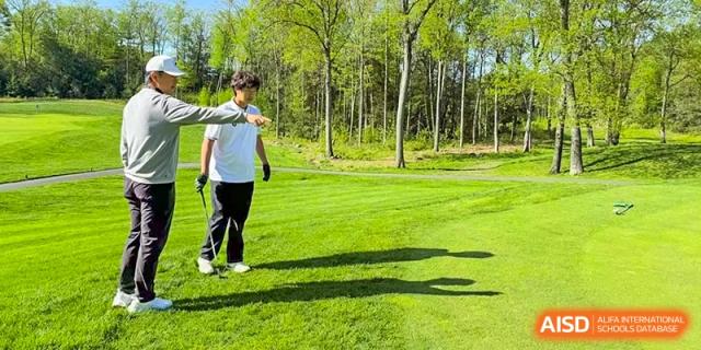 A person in white walking on a green golf course, with trees in the background at HD Qingdao School.
