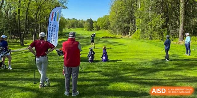 Two people on a green golf course, one in a red sweater looking at a golf bag at HD Qingdao School.