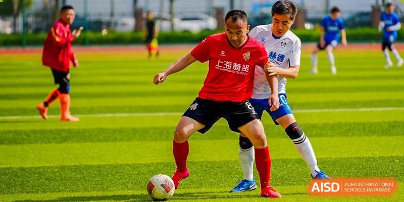 A soccer player in a red jersey dribbling a ball on a green turf field during a game at HD Qingdao School.