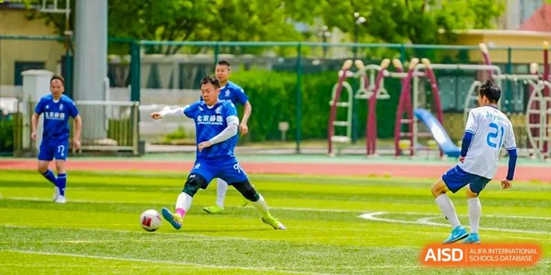 A soccer player in a blue jersey kicking a ball during a game at HD Qingdao School.