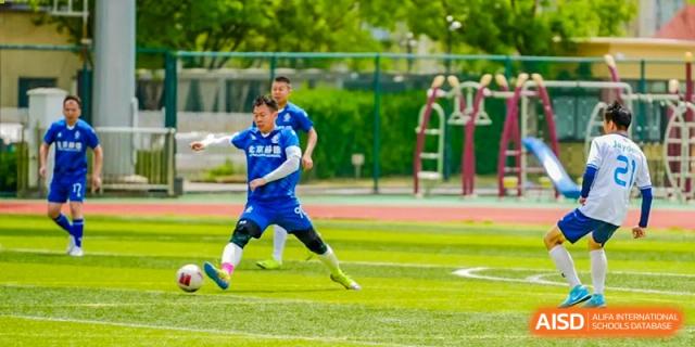 A soccer player in a blue jersey kicking a ball during a game at HD Qingdao School.