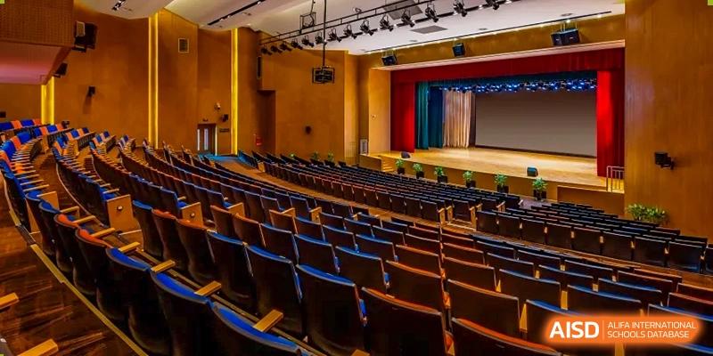 A wide shot of an empty auditorium with rows of blue seats and a stage at HD Qingdao School.
