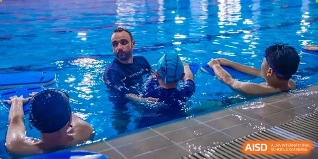 An instructor in the water teaching a child wearing goggles how to swim at HD Qingdao School.