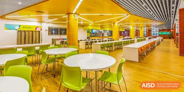 A modern cafeteria or dining area with round white tables and bright yellow chairs at HD Qingdao School.