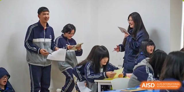 Students from Hongyi Cambridge International School (HYCIS) in their uniforms reading and discussing materials during a classroom activity.