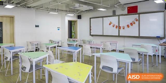 An empty, well-lit classroom at Hongyi Cambridge International School (HYCIS) with light-colored desks and chairs.