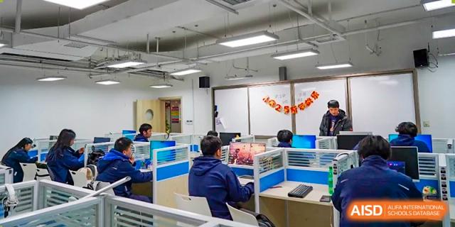 Students from Hongyi Cambridge International School (HYCIS) working independently on computers in a brightly lit lab or study area with cubicle dividers.