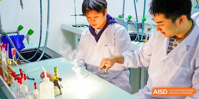 A student from Hongyi Cambridge International School (HYCIS) wearing a lab coat performing an experiment that is generating steam or smoke.