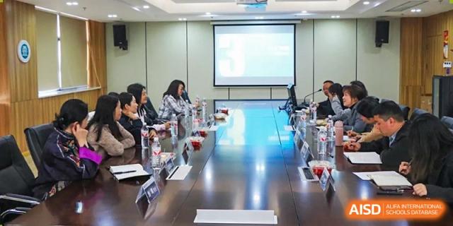 Faculty or students from Hongyi Cambridge International School (HYCIS) seated around a long, reflective table in a bright conference room for a meeting.