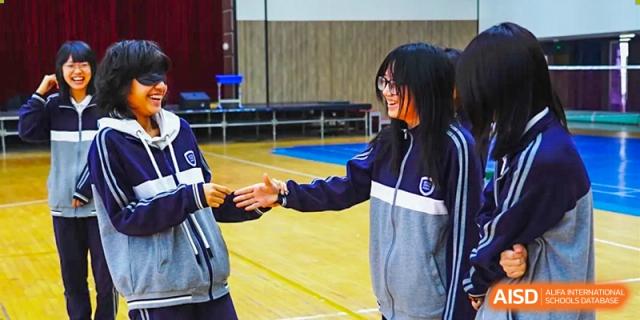Two students from Hongyi Cambridge International School (HYCIS) in their uniforms shaking hands on a sports court in a gesture of sportsmanship.