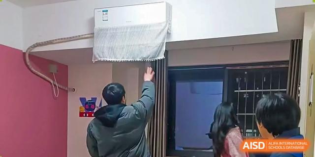 A person reaching up to adjust an air conditioning unit or a curtain over a window inside a building at Hongyi Cambridge International School (HYCIS).