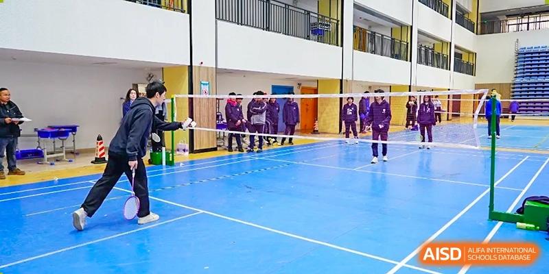 Students from Hongyi Cambridge International School (HYCIS) standing at the net on an indoor blue sports court, likely a volleyball or badminton court, inside a gymnasium.