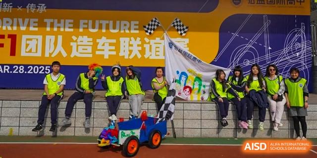 Students from Hongyi Cambridge International School (HYCIS) posing with a checkered flag and a small, colorful race car prop in front of a yellow banner during a school event or competition.