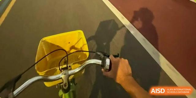A close-up shot of a hand gripping the handlebar and brake of a yellow bicycle on a sports field at Hongyi Cambridge International School (HYCIS).