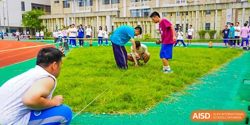 Students from Hongyi Cambridge International School (HYCIS)bending down to participate in a team game or activity on a grassy field.
