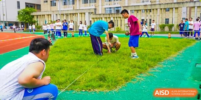 Students from Hongyi Cambridge International School (HYCIS)bending down to participate in a team game or activity on a grassy field.