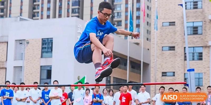A student from Hongyi Cambridge International School (HYCIS) leaping over an obstacle in mid-air during a sports day competition.