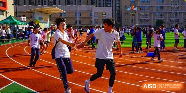 Students from Hongyi Cambridge International School (HYCIS) running a relay race on a red track, passing a baton.