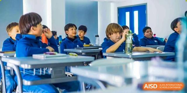 Young students look to the side while sitting at their desks in a classroom at the International School of Qingdao.