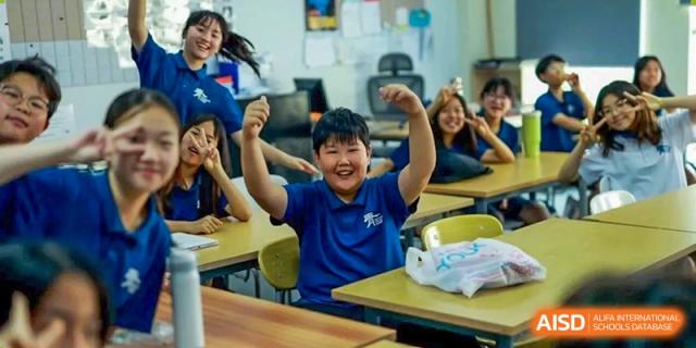 A male student raises his hands in excitement at his desk in a classroom at the International School of Qingdao.