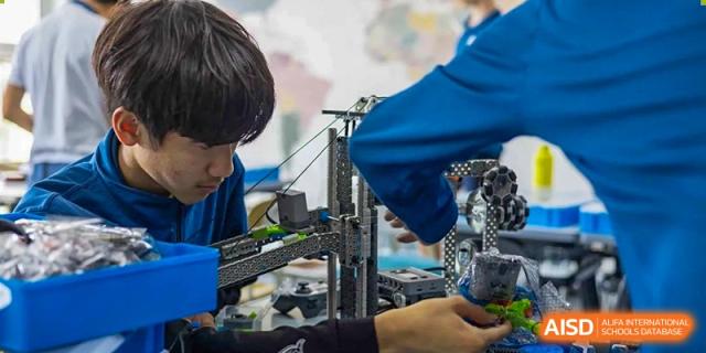 A student works on a complex robot with tools at the International School of Qingdao.