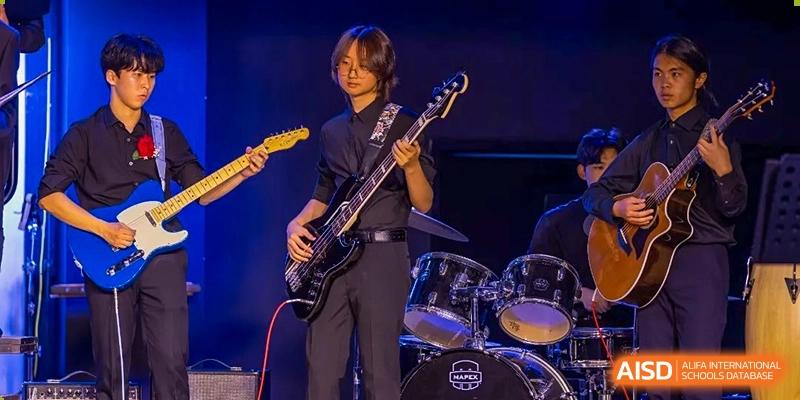 A student plays an electric bass guitar on stage with a drum set in the background at the International School of Qingdao.