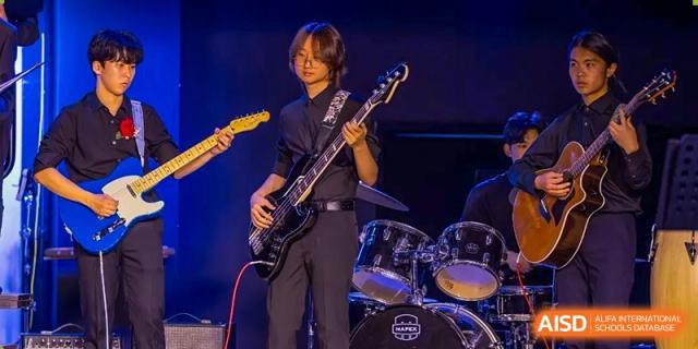 A student plays an electric bass guitar on stage with a drum set in the background at the International School of Qingdao.
