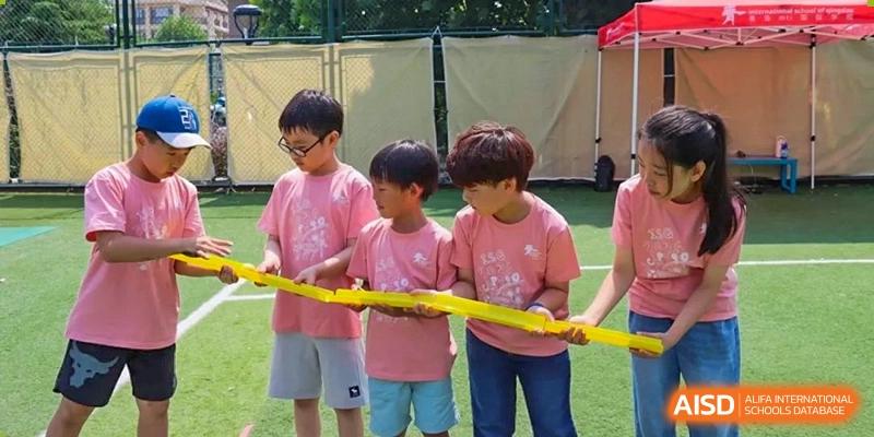Students in pink shirts hold a yellow ribbon for a race at the International School of Qingdao.