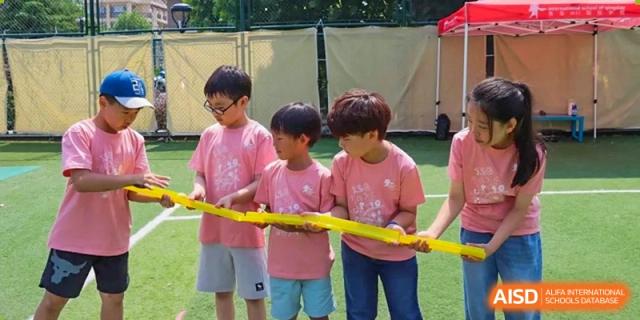 Students in pink shirts hold a yellow ribbon for a race at the International School of Qingdao.