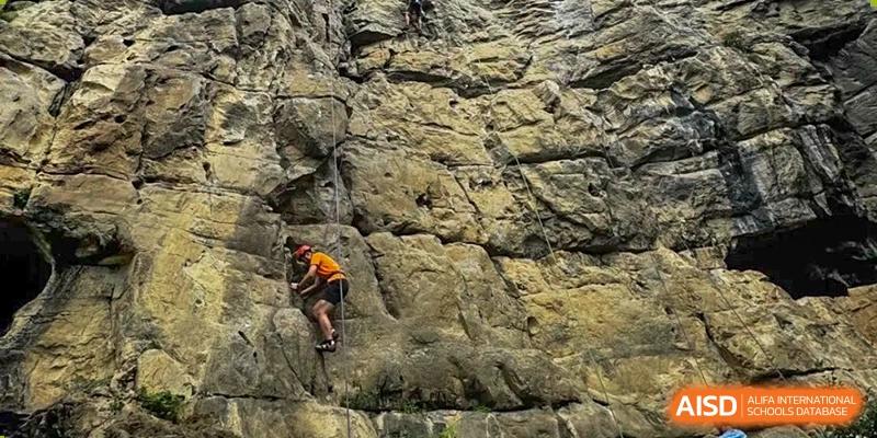 A student rock climbs on a large rock wall outdoors at the International School of Qingdao.