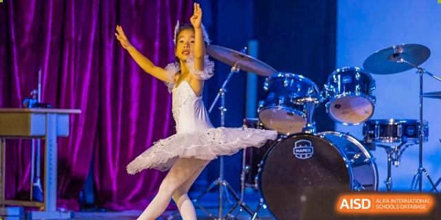 A ballerina in a white tutu performs on a stage with a drum set behind her at the International School of Qingdao.
