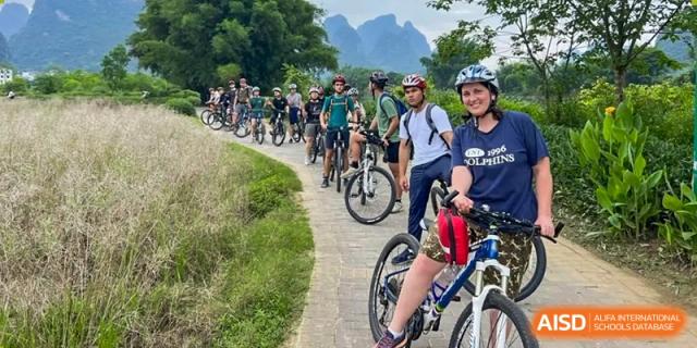 A group of students and adults rides bikes on a path at the International School of Qingdao.