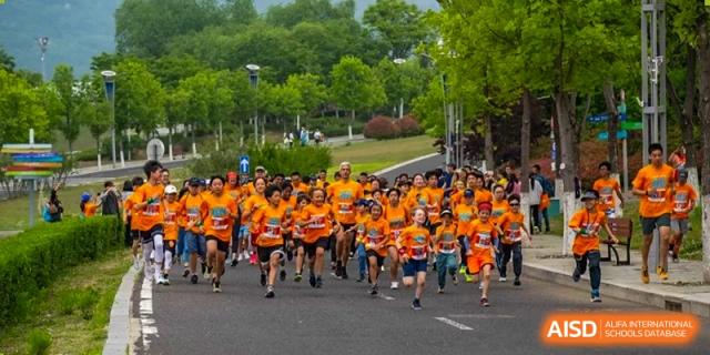 Students in orange shirts participate in a running race at the International School of Qingdao.
