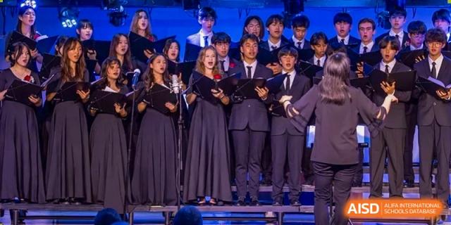 Students in choir robes sing on stage during a performance at the International School of Qingdao.