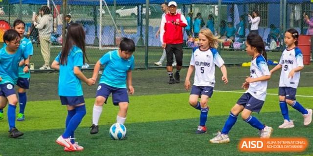 Students in blue and white jerseys play soccer on a green field at the International School of Qingdao.