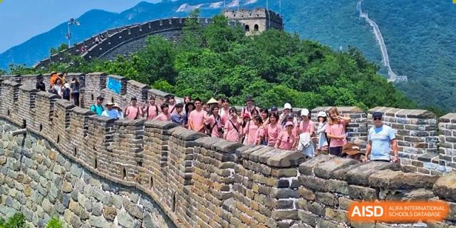 A group of students stands on a stone wall overlooking a scenic view at the International School of Qingdao.