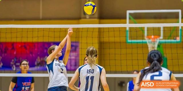 A female volleyball player in a white and blue jersey gets ready to serve at the International School of Qingdao.