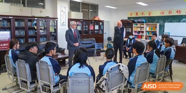 Students in a classroom listening to two visiting male speakers in suits at the International Department of Kunming No.10 Middle School.