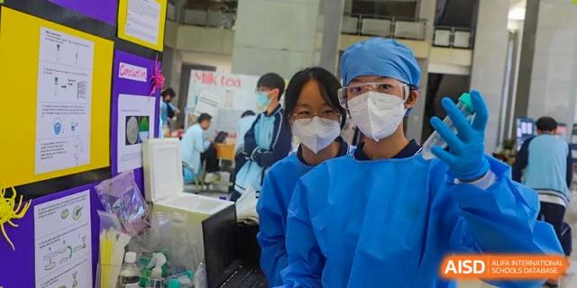 Two students in blue lab gowns and masks posing at a science exhibition at the International Department of Kunming No.10 Middle School.